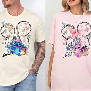 May include: Two t-shirts, one cream and one pink, featuring a cartoon design. The design includes a castle, fireworks, and a character named Stitch on the cream shirt and Angel on the pink shirt, all within a Mickey Mouse outline.