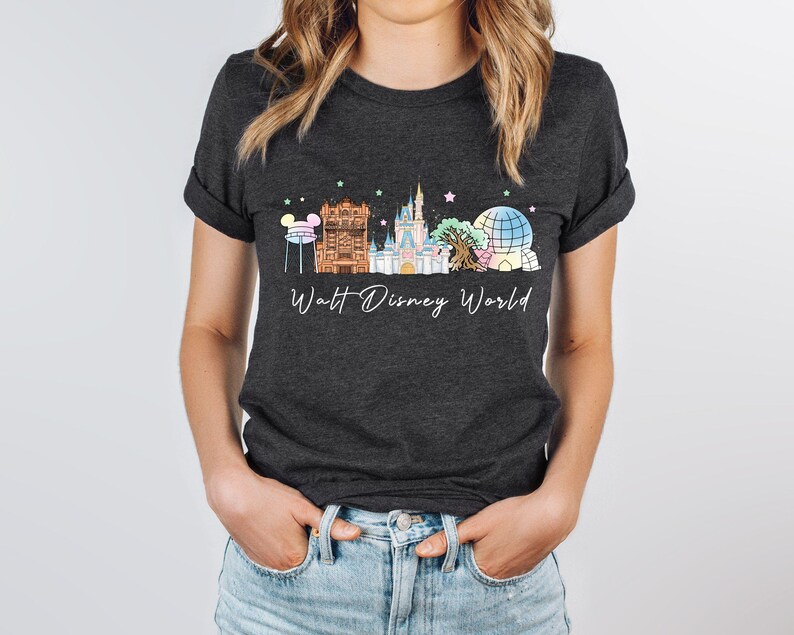 May include: A dark charcoal gray short-sleeve t-shirt featuring a graphic of the Walt Disney World skyline, including the castle, iconic park structures, and colorful stars. The text Walt Disney World is printed in white script below the graphic.
