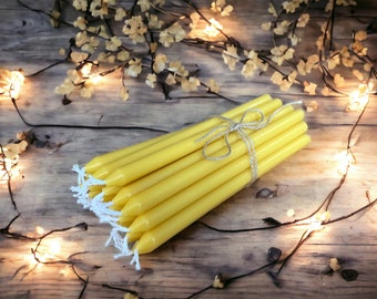 May include: A bundle of yellow beeswax candles tied together with twine. The candles are arranged in a fan shape and are sitting on a wooden surface.