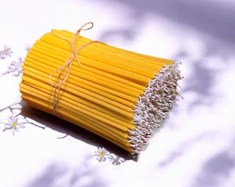 May include: A bundle of thin, yellow beeswax candles tied together with twine. The candles are arranged in a cylindrical shape and have white wicks.