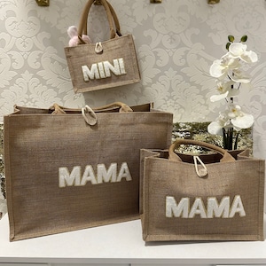 Könnte beinhalten: Drei braune Jute-Tragetaschen mit weißen, flauschigen Buchstaben. Die größte Tasche sagt "MAMA", die mittlere Tasche sagt "MAMA" und die kleinste Tasche sagt "MINI".
