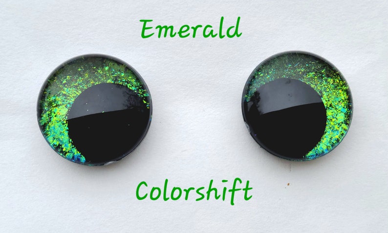 May include: Two round, black-backed, glass eyes with a green and blue iridescent color shift. The eyes are labeled "Emerald" and "Colorshift".