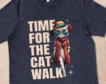 May include: A dark navy blue t-shirt featuring a graphic of a white cat wearing a colorful hat, sunglasses, and a trench coat, with the text TIME FOR THE CAT WALK printed in large cream-colored letters next to the cat illustration.