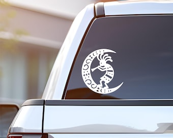May include: White Kokopelli design sticker on a car window. The sticker features a stylized figure playing a flute, set within a crescent moon shape. The design is a silhouette, with intricate cut-out details.