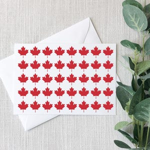 May include: A rectangular white greeting card featuring a repeating pattern of small red maple leaf icons arranged in five horizontal rows. The card is positioned on top of a plain white envelope, creating a clean and simple stationery set.