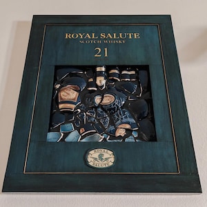May include: A rectangular dark teal wooden wall art piece featuring the text ROYAL SALUTE SCOTCH WHISKY 21. The centre contains a mosaic of broken dark blue ceramic shards from a whisky bottle, with a small oval Royal Salute logo at the bottom.