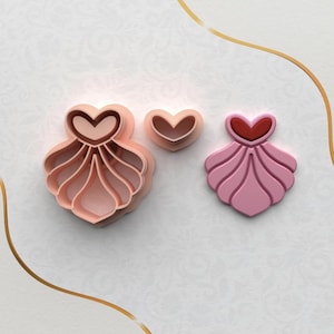 May include: Three pink heart-shaped cookie cutters. The largest cutter has a heart top and a scalloped bottom. The medium cutter is a simple heart shape. The smallest cutter has a heart top and a scalloped bottom.