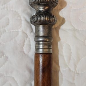 Può includere: Un bastone da passeggio in legno con una parte superiore in argento. La parte superiore presenta disegni intricati ed è composta da tre sezioni.