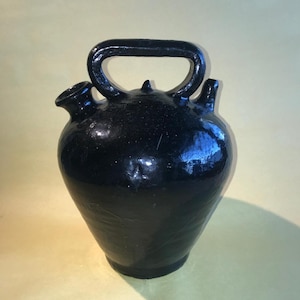 May include: A black ceramic pitcher with a handle and a spout. The pitcher has a glossy finish and a rounded shape.