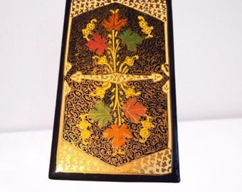 Pode incluir: Uma caixa decorativa retangular preta com um design floral. A caixa apresenta uma borda dourada e um padrão detalhado. O design central inclui folhas coloridas em vermelho, laranja e verde, com detalhes dourados. A caixa tem um acabamento brilhante.