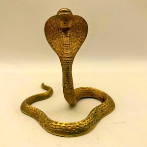 May include: A golden cobra statue with a detailed, textured surface. The snake is posed in a striking, upright position, with its hood flared. The sculpture is made of a shiny, metallic material, and the details are well-defined.