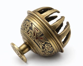 Könnte beinhalten: Eine Messing-Schelle mit kugelförmigem Körper, verziert mit schwarzen, geätzten Blumenmustern und einem kleinen runden Sockel. Der obere Teil der Glocke hat vertikale Ausschnitte und die Metalloberfläche besitzt ein antikes Gold-Finish.