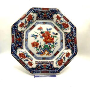 May include: An octagonal decorative plate with a floral design. The plate features a white center with red and orange flowers, a blue bird, and green leaves. The border is blue, red, and white with floral and geometric patterns.