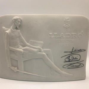 Puede incluir: Escultura de cerámica blanca que representa una figura sentada con una espada, leyendo un libro. La escultura tiene el texto "LLADRO COLLECTOR SOCIETY" y firmas. La figura lleva un traje de época.