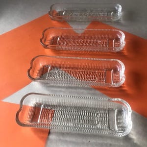 May include: Four clear glass dishes with a textured surface. The dishes are rectangular and have a slight curve to them. They are stacked on top of each other.