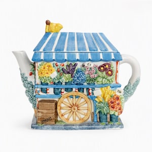 Op de afbeelding: Een keramische theepot in de vorm van een bloemenkraam met een blauw-wit gestreept dak. De kraam heeft kleurrijke gebeeldhouwde bloemen, een houten kist met het label FRESH en prijskaartjes met £1 en 70p. Witte tuit en handvat.