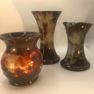 May include: Three ceramic vases in varying shapes and sizes. The vases have a glossy finish with brown, orange, and cream colour gradients. The tallest vase is approximately 25 cm tall, while the shortest is about 15 cm.
