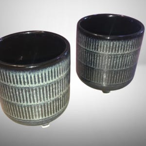 Op de afbeelding: Twee zwarte en grijze keramische potten met een textuurontwerp. De potten zijn rond en hebben een brede basis.