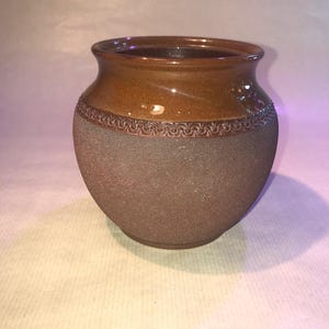 May include: A brown ceramic pot with a textured surface and a decorative band around the top.