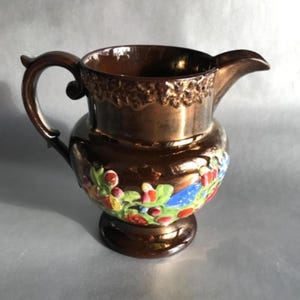 May include: A brown ceramic jug with a copper glaze and floral designs in shades of red, green, blue, and yellow.