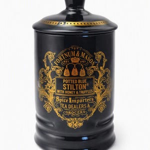 Puede incluir: Un recipiente de cerámica negra con tapa a juego, que presenta texto impreso en oro y diseños de filigrana ornamentados. La etiqueta dice Fortnum & Mason, Est. 1707, Potted Blue Stilton with Honey & Truffles, Spice Importers, Tea Dealers & Grocers.