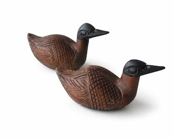 Puede incluir: Dos figuras de patos de madera tallada con cabezas y picos negros lisos junto a cuerpos marrones texturizados. Las alas y los costados de cada pato muestran intrincados patrones de rejilla y plumas tallados directamente en la madera.