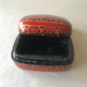 May include: A small, red and black paper mache box with a floral design. The box is open and the inside is black.