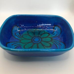Puede incluir: Un cuenco rectangular de cerámica con un exterior azul vibrante y un diseño floral en tonos turquesa y azul en el interior. El cuenco tiene esquinas redondeadas y un acabado brillante, adecuado para servir o exhibir.