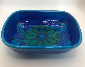 May include: A rectangular ceramic bowl with a vibrant blue exterior and a floral design in shades of teal and blue on the interior. The bowl has rounded corners and a glossy finish, suitable for serving or display.