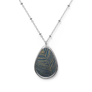 May include: Silver-toned necklace with a teardrop pendant. The pendant features a blue and gold leaf-like pattern encased in a silver frame. The chain is delicate, with small beaded accents.