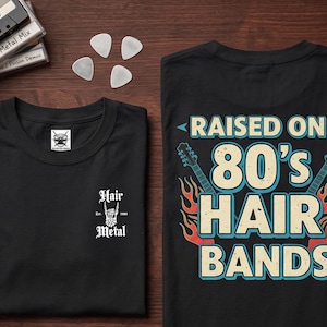 May include: A black t-shirt featuring a small white graphic on the front chest that reads Hair Metal Est. 1980. The back of the shirt displays a large graphic with the text RAISED ON 80'S HAIR BANDS, flanked by two electric guitars and flames.
