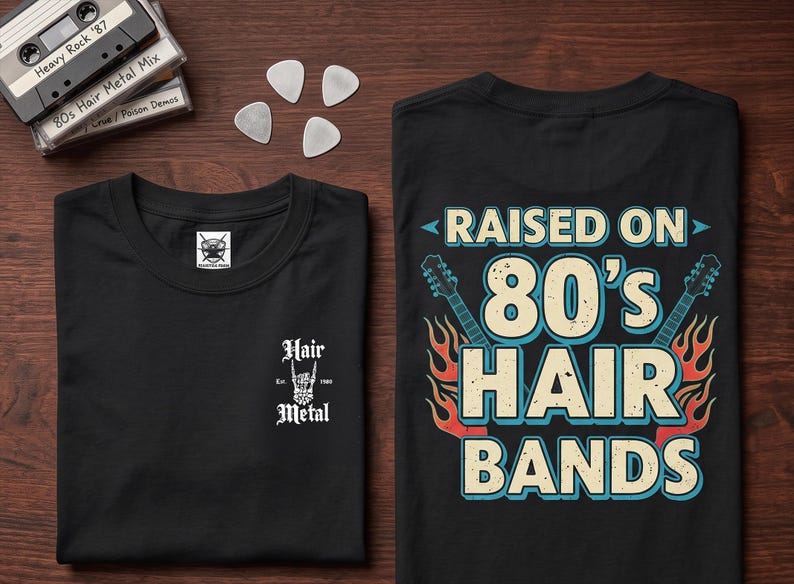 May include: A black t-shirt featuring a small white graphic on the front chest that reads Hair Metal Est. 1980. The back of the shirt displays a large graphic with the text RAISED ON 80'S HAIR BANDS, flanked by two electric guitars and flames.