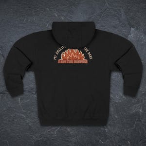 May include: A black hooded sweatshirt featuring a graphic on the back. The design displays a stylized orange and red bonfire with the text "MY ANCESTORS THE DARK" arched above and "I AM THE BONFIRE" printed in a rectangular box below the flames.
