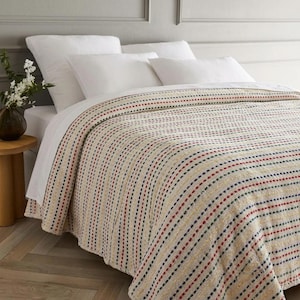 Puede incluir: Un edredón a rayas beige y blanco con detalles de puntos rojos, azules y amarillos. El edredón está sobre una cama con sábanas y almohadas blancas. La habitación está bien iluminada.