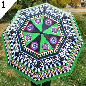 May include: A green, black, white, and multi-colored umbrella with a geometric pattern. The umbrella has a black handle and is open.