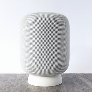 Puede incluir: Un altavoz inteligente cilíndrico blanco con una rejilla de malla y una base blanca.