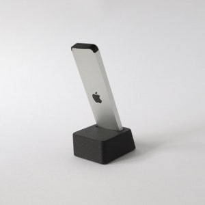 May include: A silver Apple remote control with a black top and an Apple logo on the front, sitting on a black charging dock.