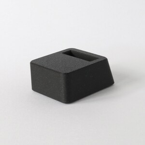 May include: A black, rectangular, textured,  stand with a slot in the top.