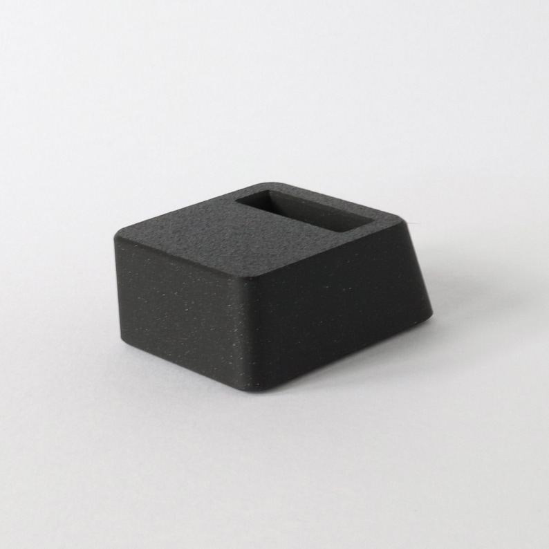 May include: A black, rectangular, textured,  stand with a slot in the top.