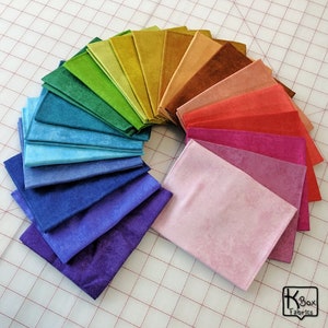 May include: A vibrant display of fabric swatches arranged in a semi-circle, showcasing a spectrum of colors. The collection includes shades of purple, blue, green, yellow, orange, and pink. The fabric appears to have a soft, velvety texture, perfect for crafting projects.