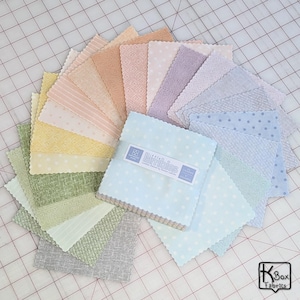 May include: A collection of pastel-colored fabric squares arranged in a circular pattern. The fabrics include various patterns like polka dots, stripes, and textured weaves. A stack of light blue fabric squares with the text "Littlefield Lambies" is in the center.