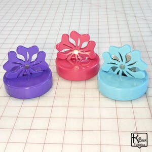 May include: Three magnetic bottle stoppers with snowflake designs. The stoppers are purple, pink, and blue.