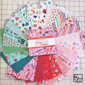 May include: A collection of colorful fabric squares with various patterns, including candies, hearts, and strawberries. The fabric squares are arranged in a circular pattern. The center features a package labeled "Sweet Shoppe".
