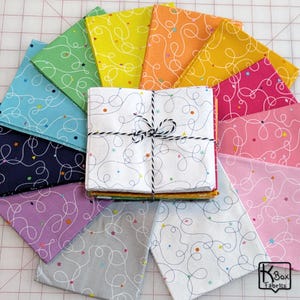 May include: A collection of colorful fabric squares arranged in a circular pattern. Each square features a white, swirling line design with small stars and dots. The fabric bundle in the center is tied with black and white twine. The color palette includes shades of blue, green, yellow, pink, and purple.