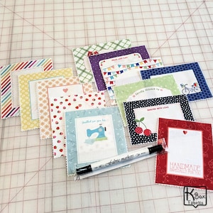 May include: A collection of fabric markers and decorative fabric labels with various patterns and text. The labels feature designs like strawberries, sewing machines, and bicycles. The text includes phrases like "Handmade Especially for You" and "Quilted with Love."