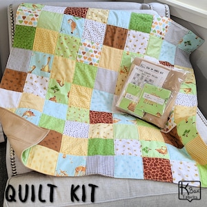 May include: A patchwork quilt featuring a grid of squares with giraffe, heart, and geometric patterns in shades of green, yellow, brown, and blue. A clear plastic package labeled My First Scrappy Patchy Quilt Kit sits on top of the fabric squares.