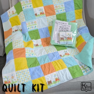 May include: A colorful patchwork quilt kit with squares of yellow, green, blue, and orange fabric. The quilt features animal and floral patterns. The words "QUILT KIT" are printed on the quilt. A package containing instructions and fabric is on top.