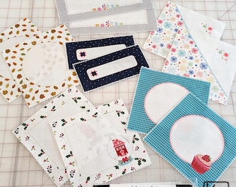 12 etiquetas para colchas con 6 diseños de la tela "Stitched With Love" de Kimberbell y 1 marcador permanente de tela negro. Etiquetas de tela para coser en colchas.