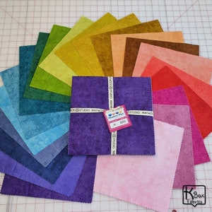 May include: A collection of fabric squares in a rainbow of colors, arranged in a semi-circle. The central stack of purple squares is tied with a ribbon that reads "MAYWOOD STUDIO". A tag on the stack reads "Shadow Play". The fabric has a textured appearance.