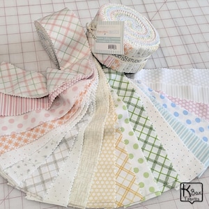 May include: A collection of fabric strips in various pastel patterns, including plaid, polka dots, and stripes. A rolled bundle of fabric sits atop the spread-out strips. The fabrics are in shades of pink, green, yellow, and blue.